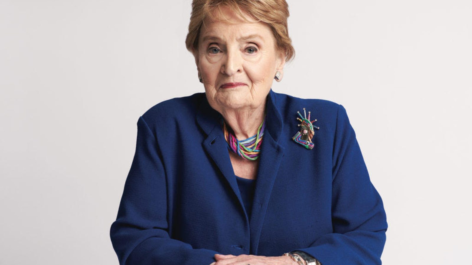 Madeleine Albright in a navy suit with a colorful necklace and blonde hair
