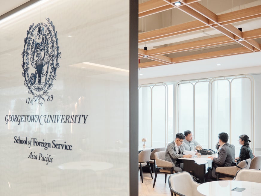 Four students sitting across from each other, while speaking and browsing papers.