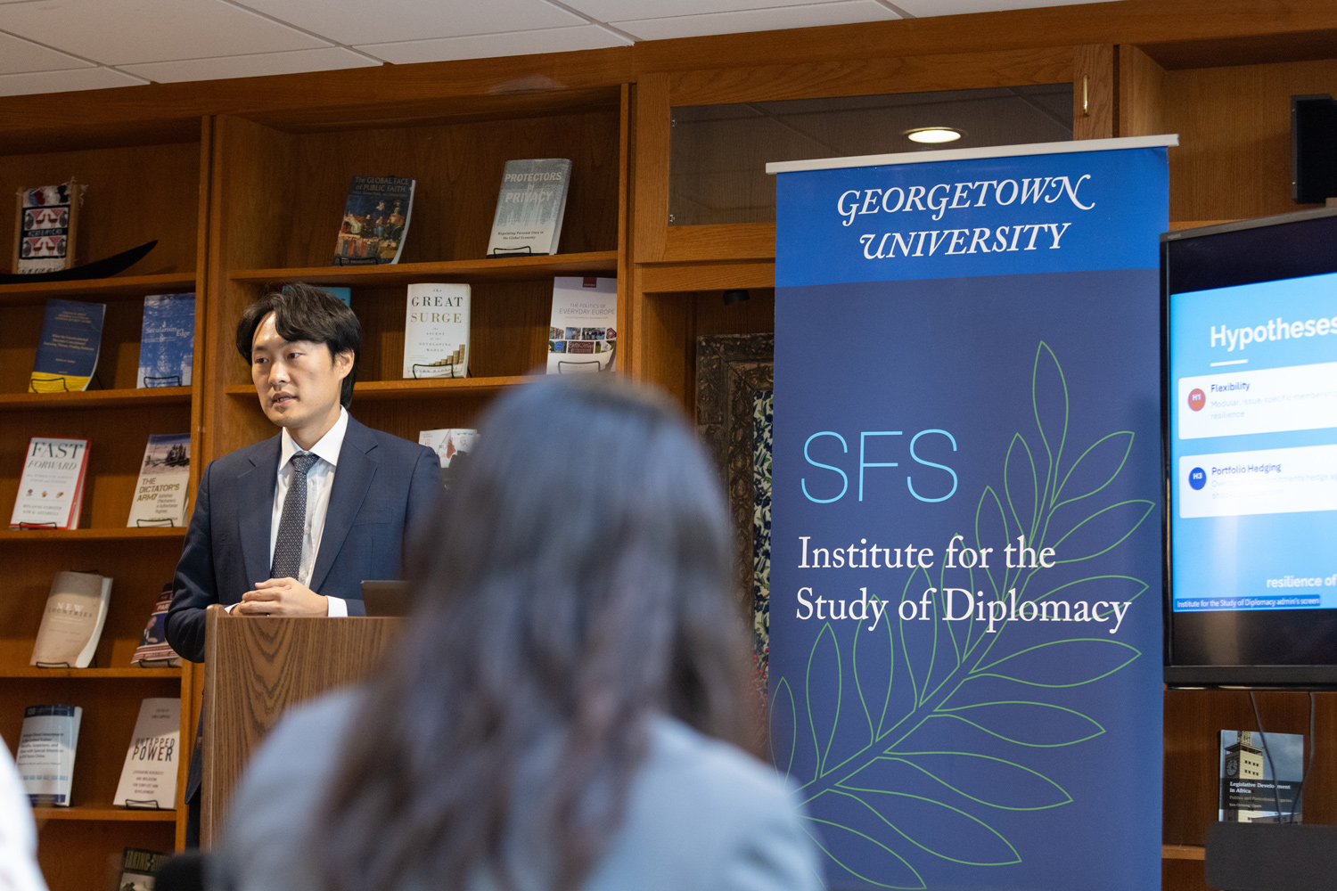 Man speaking from a podium, presenting slides on a screen