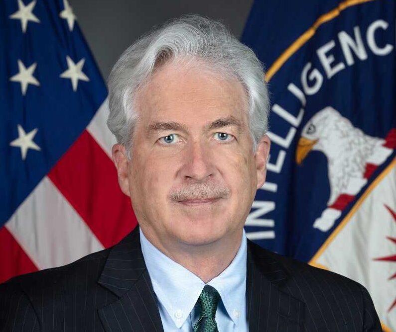 Burns in a suit with the US and CIA flags behind him.